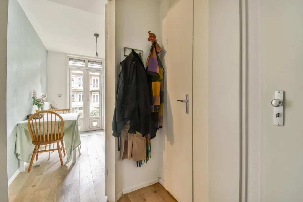 L’ingresso di un appartamento: cappotti e sciarpe appesi accanto alla porta, in fondo il tavolo della cucina.