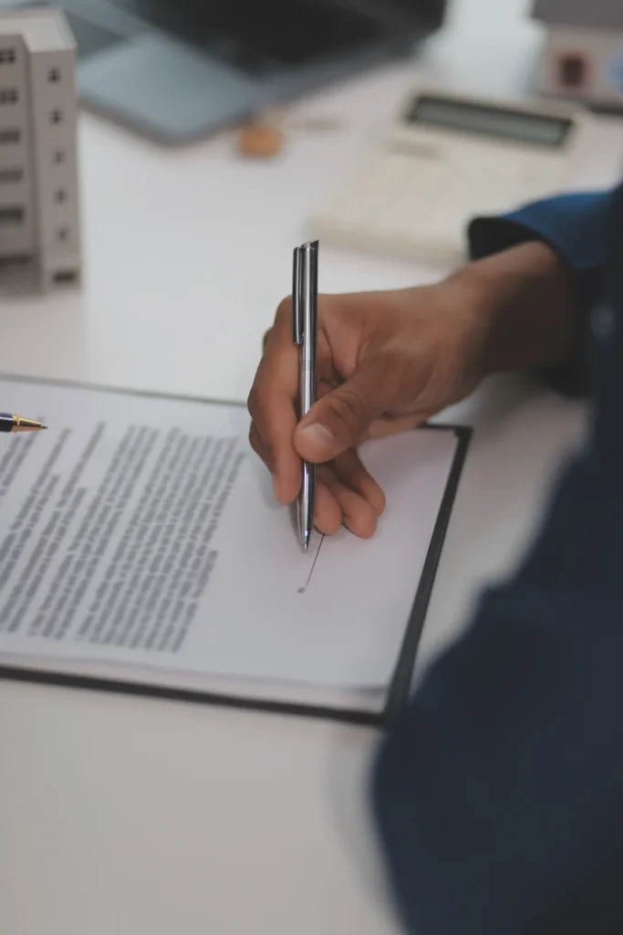 Una mano firma con la penna un documento appoggiato su una cartellina, su una scrivania chiara.
