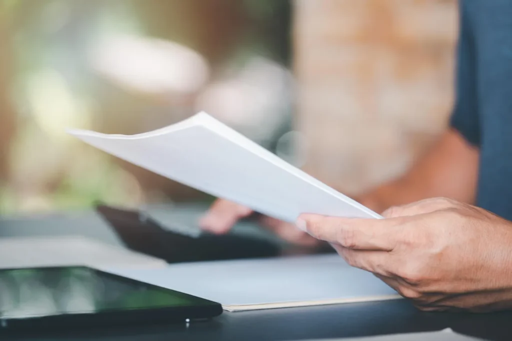 Due mani che tengono un documento di alcune pagine, letto con attenzione a un tavolo.