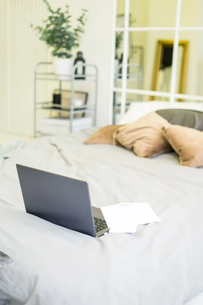 Un portatile aperto e alcuni fogli appoggiati su un letto, in una stanza di casa.